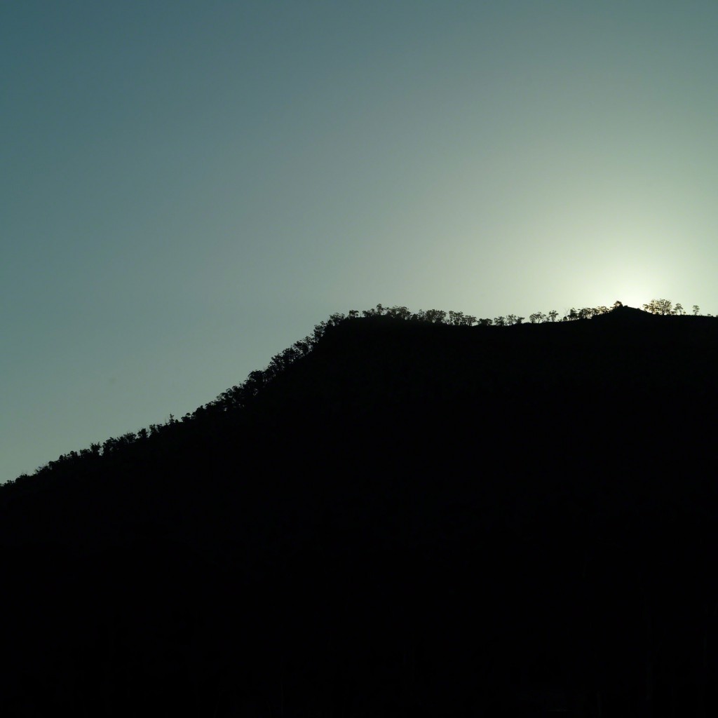 Sun setting behind tree lined hill